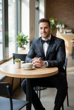 Amsterdam Tuxedo Jacket Peak worn by man at cafe; black peak-lapel tuxedo with bow tie.