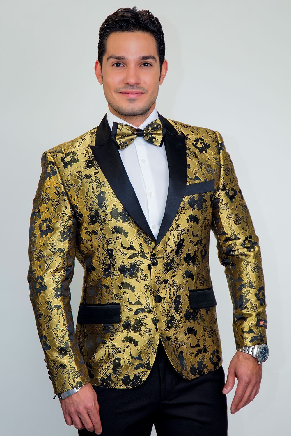 Male model wearing Amsterdam peak-lapel gold floral tuxedo jacket, black satin lapels, white shirt, bow tie.